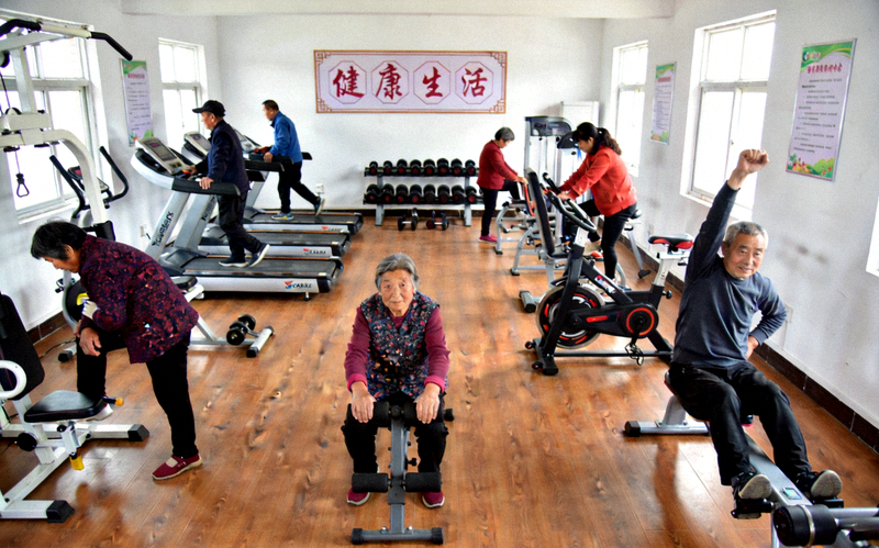 乡村百姓健身房内部 - 村民在专业器械上进行锻炼，环境明亮整洁