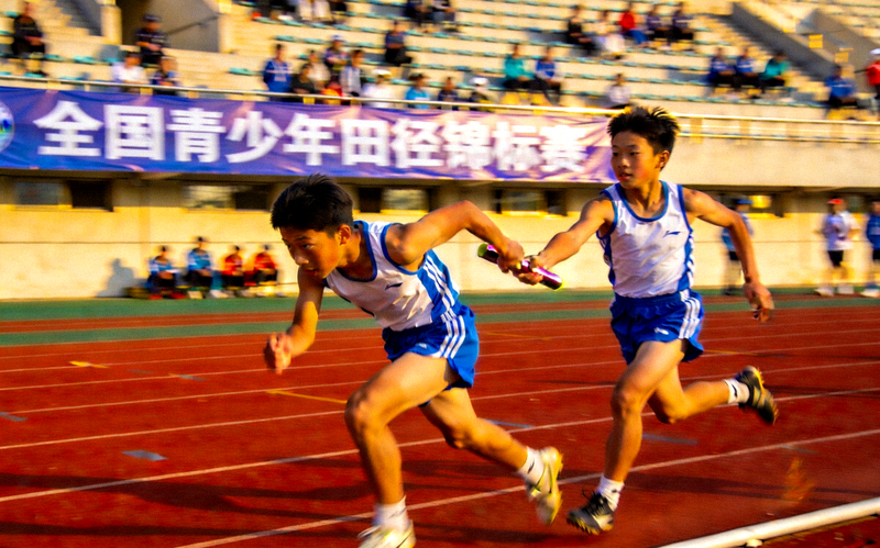 全国青少年田径锦标赛现场 - 田径赛道上运动员交接接力棒的紧张瞬间