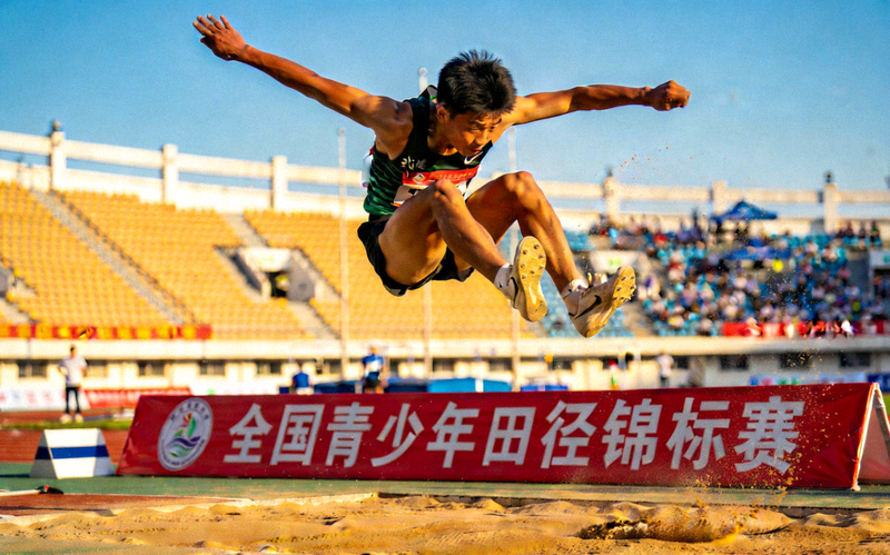 全国青少年田径锦标赛回顾 - 青少年跳远选手在沙坑前腾空跃起的精彩镜头