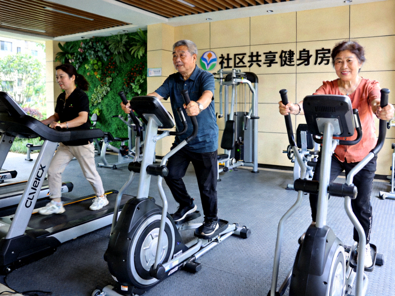 社区共享健身房照片 - 居民使用跑步机与力量器械进行锻炼，器械排列整齐
